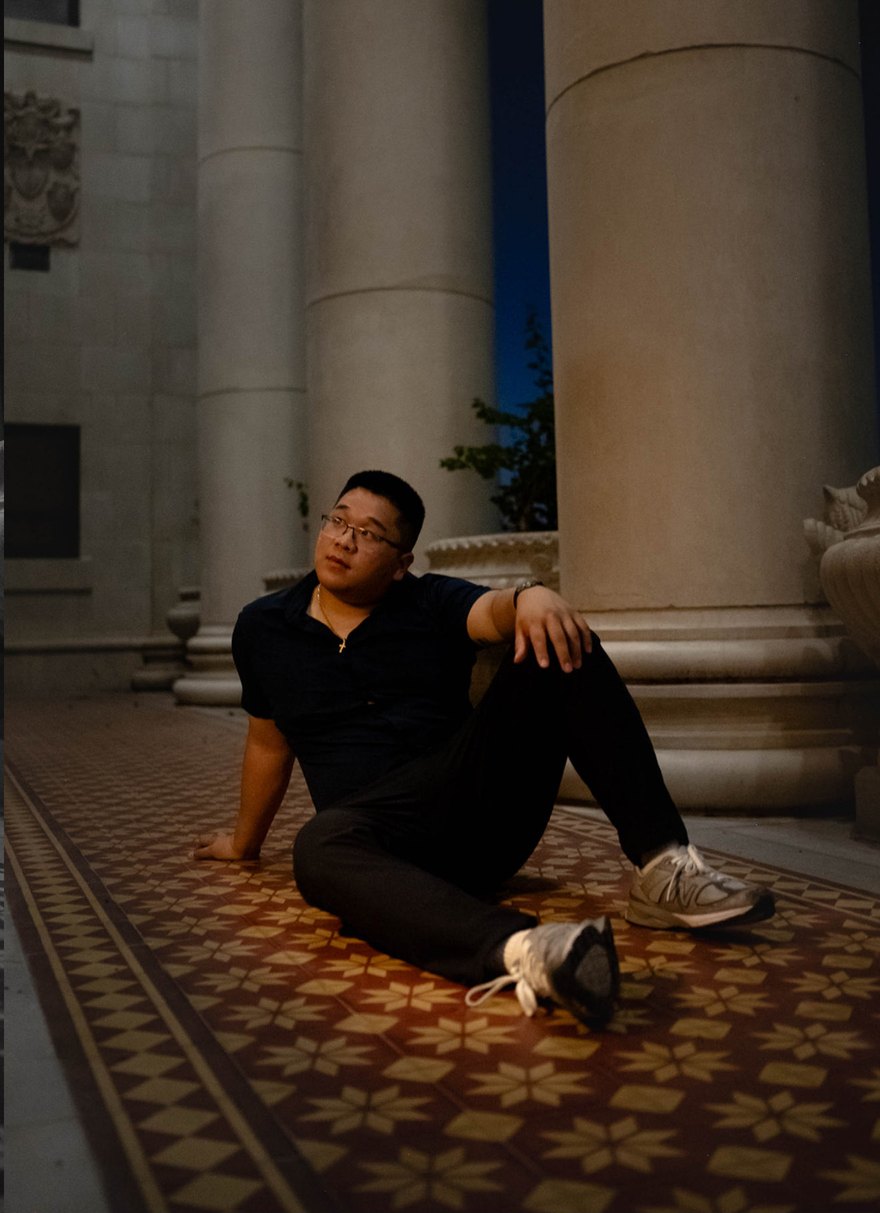 Aaron Wang seated on a patterned tile floor between stone columns at dusk