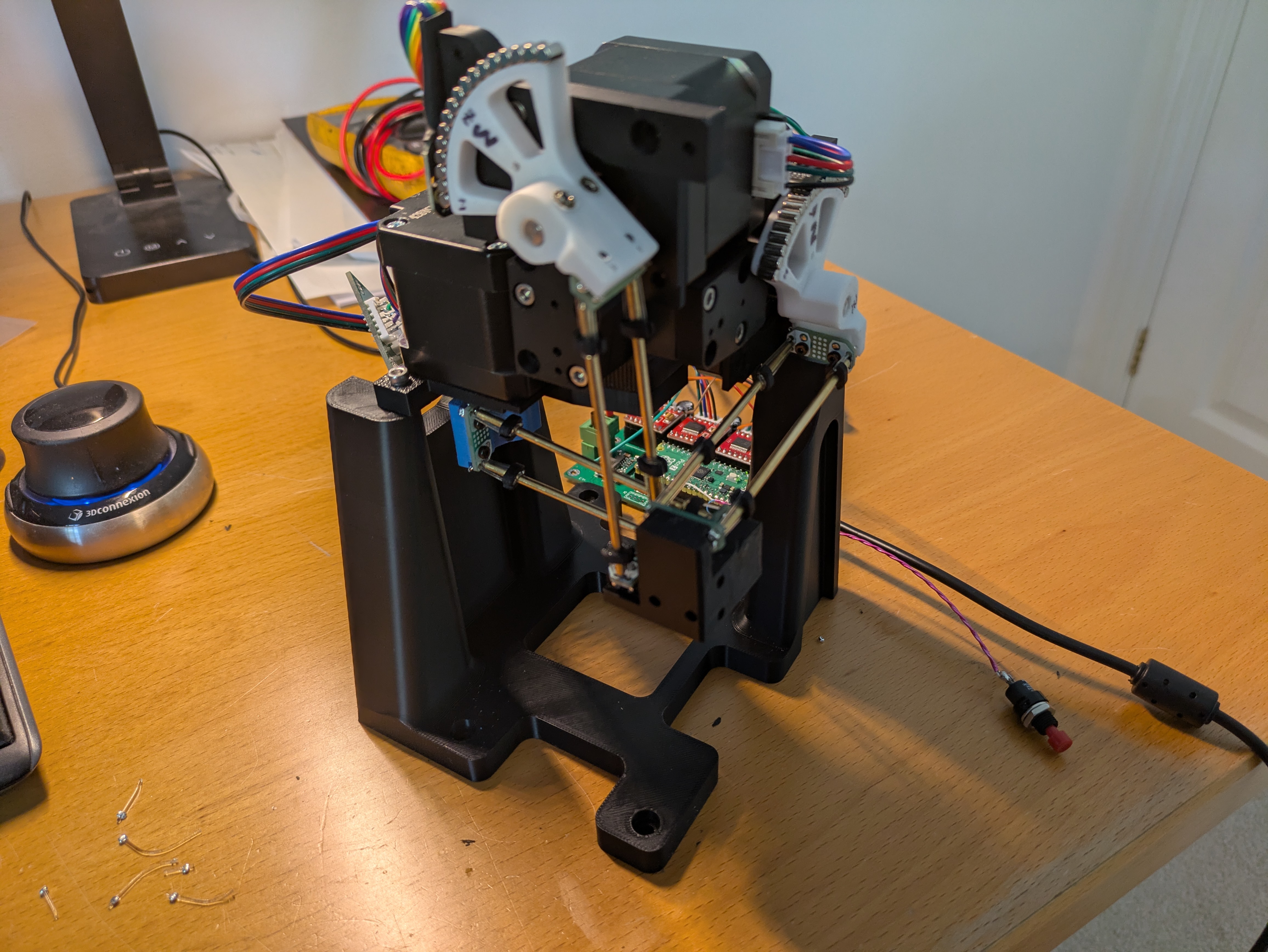 Our assembled Open Micro-Manipulator on a desk: black printed frame, three stepper motors with white printed flexure arms, and a Raspberry Pi microcontroller board with stepper drivers.